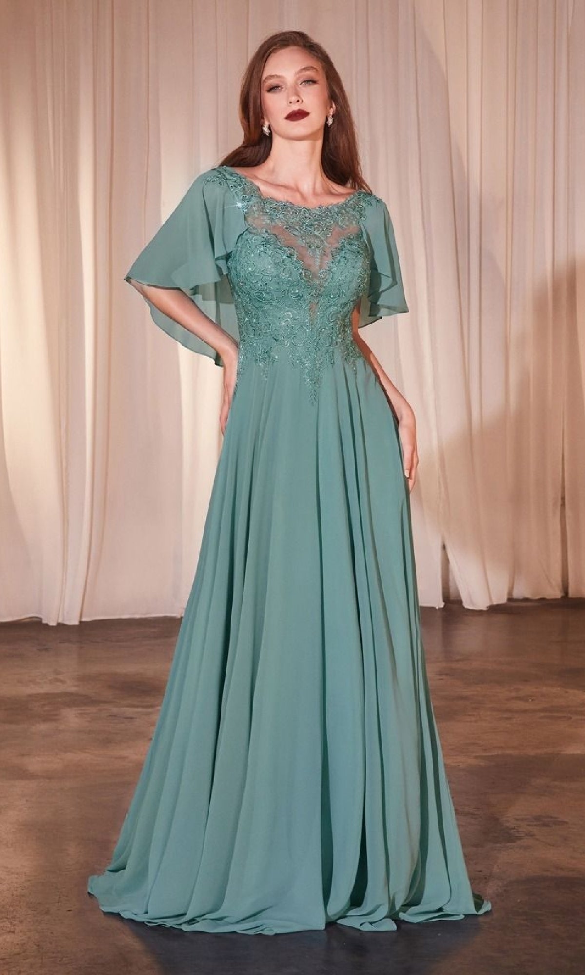 A woman stands against a neutral curtain backdrop wearing the Cape-Sleeve Long A-Line Prom Dress: Ladivine HT101, a floor-length seafoam green chiffon gown with lace bodice detailing and sheer cape sleeves.